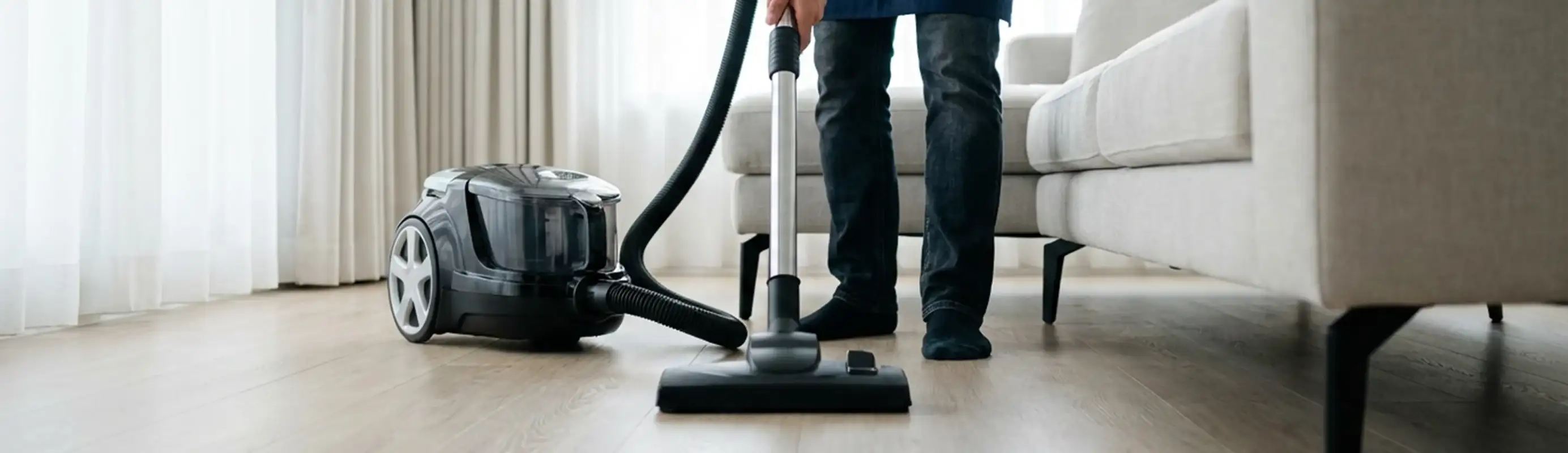 Professional house cleaner vacuuming a living room floor with a canister vacuum cleaner, Glendale, AZ.