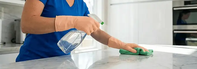 Maid service worker spraying and wiping a kitchen countertop with a microfiber cloth for sanitizing, Glendale, AZ.