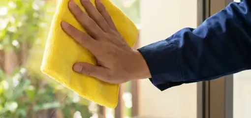 House cleaner wiping a glass window with a yellow microfiber cloth for streak-free cleaning, Glendale, AZ.